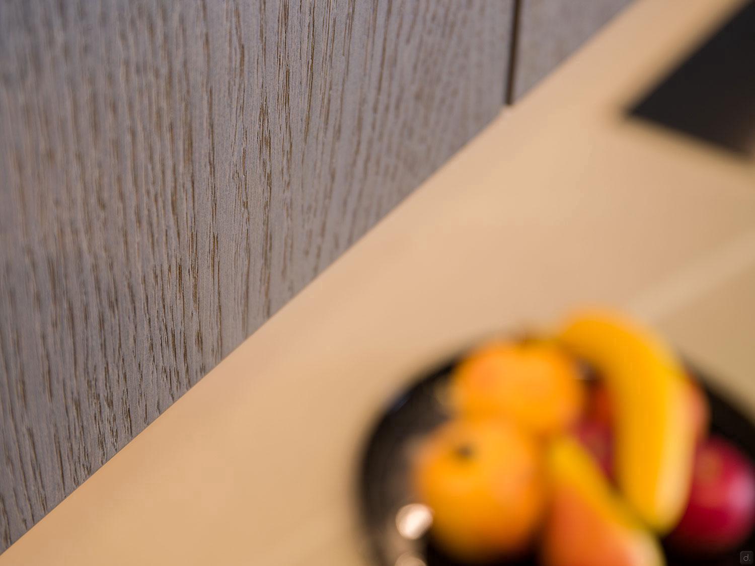 A textured wooden surface appears on the left, with a blurred plate of assorted fruits in the lower right—an ideal accent for stylish homes featuring Modern Kitchens by ORDER Kitchen Furniture.
