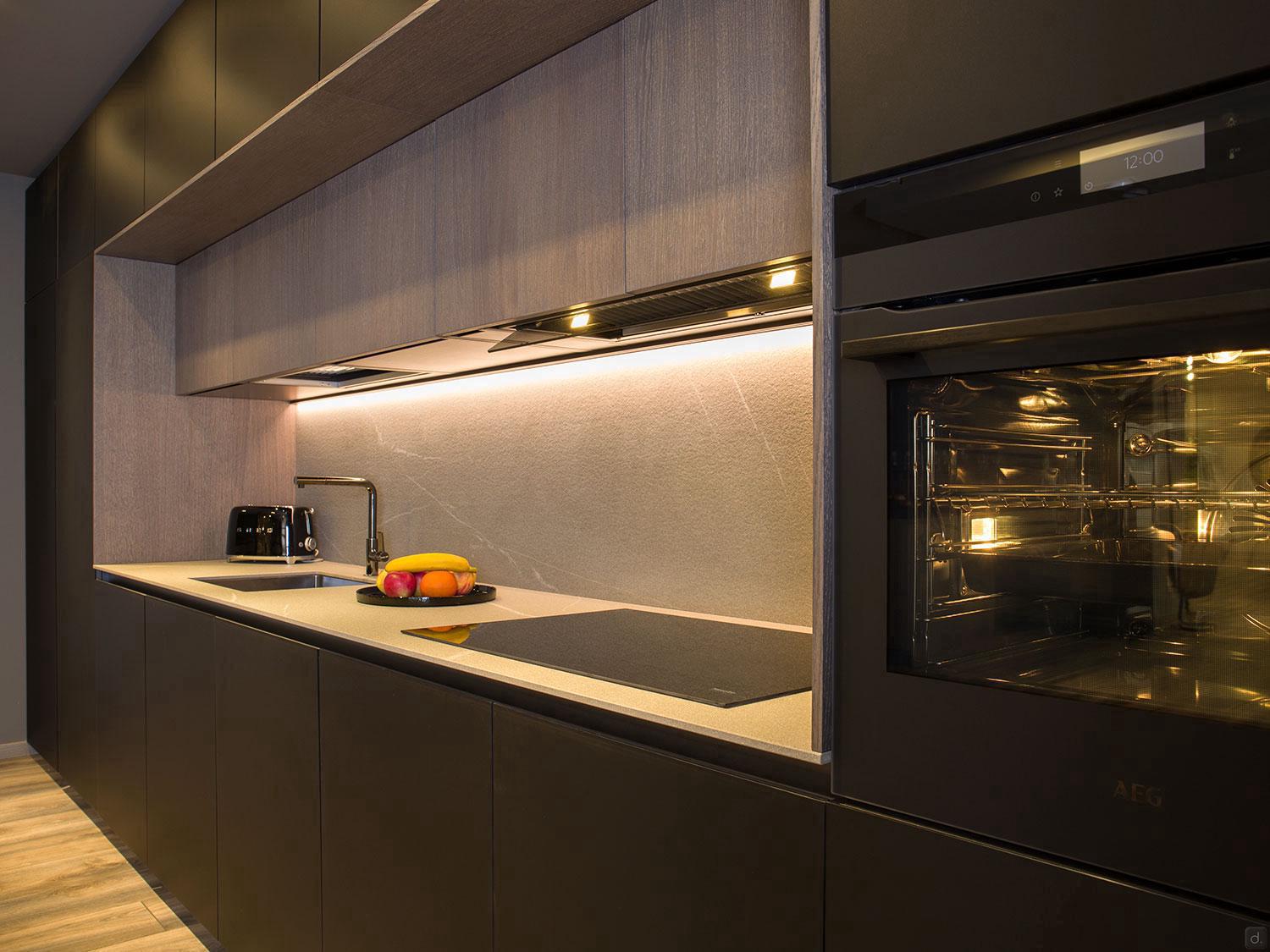 Experience Modern Kitchens by ORDER Kitchen Furniture in Yerevan, featuring dark cabinets, built-in oven, induction cooktop, under-cabinet lighting, sink, toaster, fruit bowl on the counter, and custom minimalist design.