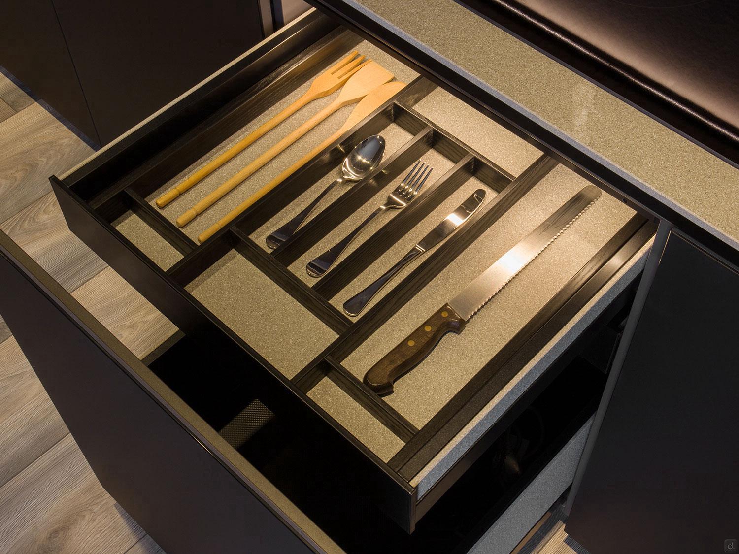 Open a kitchen drawer from the ORDER Kitchen Furniture Modern Kitchens line, revealing organized utensils—wooden spoons, metal spoon, fork, knife, and bread knife—all neatly arranged in a sleek compartment tray.