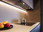 Modern Kitchens by ORDER Kitchen Furniture in Yerevan feature an induction cooktop, a stainless steel pot, and a black fruit tray on the counter, all highlighted by warm under-cabinet lighting and stylish custom cabinetry.