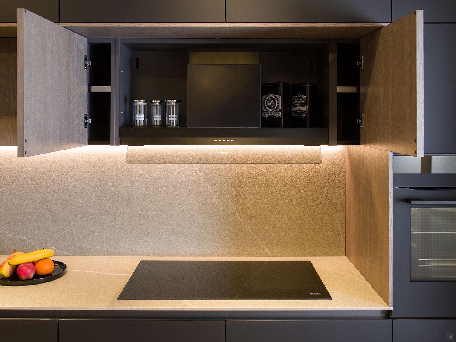 The Modern Kitchens by ORDER Kitchen Furniture in Yerevan showcases wooden cabinets above an induction cooktop, open to show spice jars and coffee containers, with a fruit bowl on the countertop and soft lighting highlighting the backsplash.