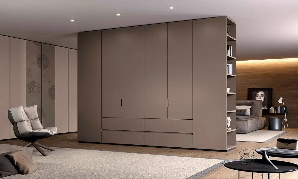 A modern living space features a large, taupe-colored wardrobe with sleek doors and built-in shelving on the side. Minimalist furniture and soft lighting complement kitchen cabinets Yerevan-style for a stylish, cozy atmosphere.