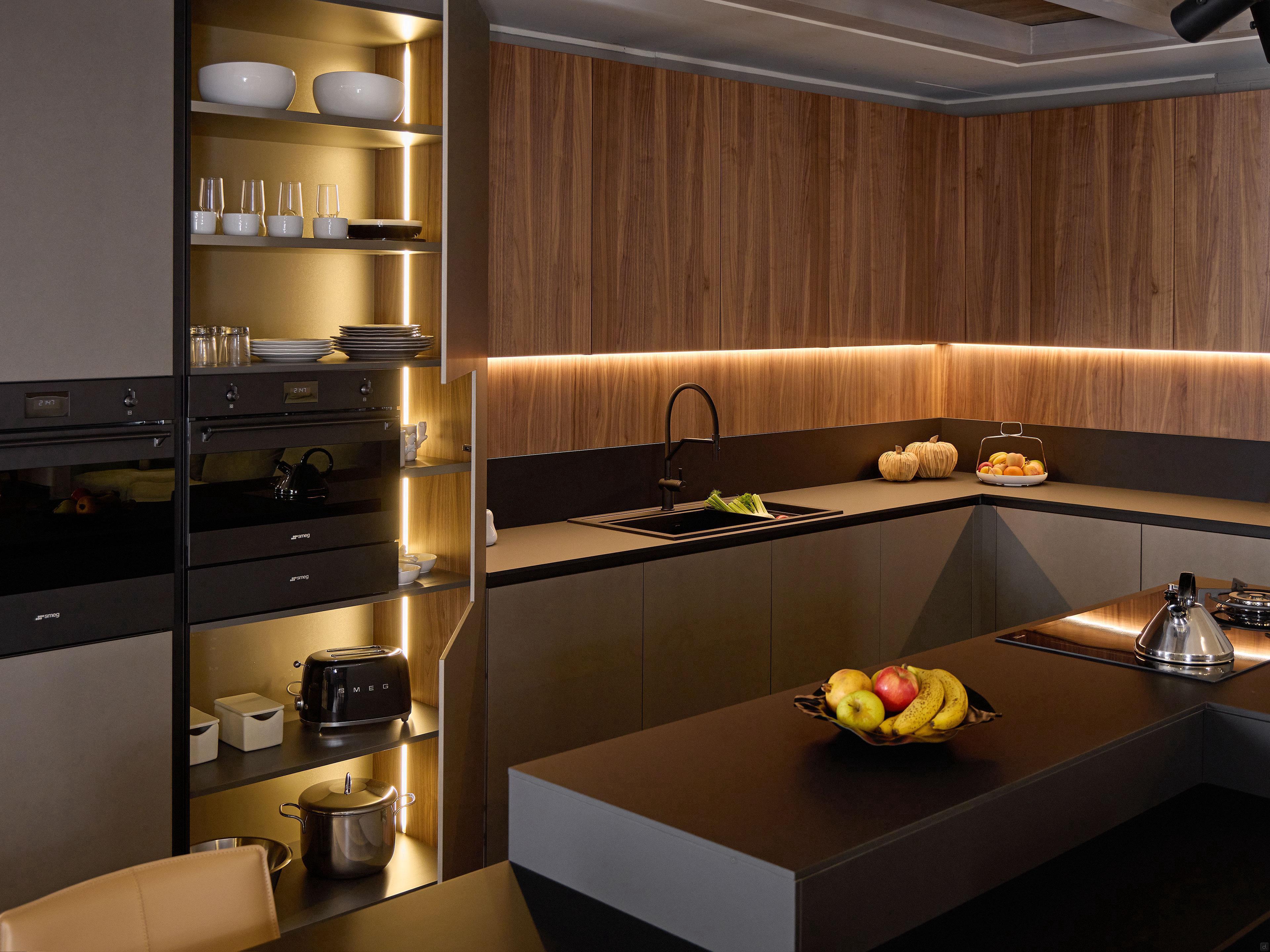 Modern Kitchens by Kitchen Furniture in Yerevan feature wood-paneled cabinets, built-in ovens, open shelving, under-cabinet lighting, a black sink, fruit bowls, and a cooktop on a dark island countertop.