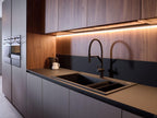 Modern Kitchens by Kitchen Furniture feature sleek wood cabinets, a matte black countertop, built-in ovens, and an integrated black sink with curved faucet—ideal inspiration for lovers of modern kitchens and custom kitchen furniture.