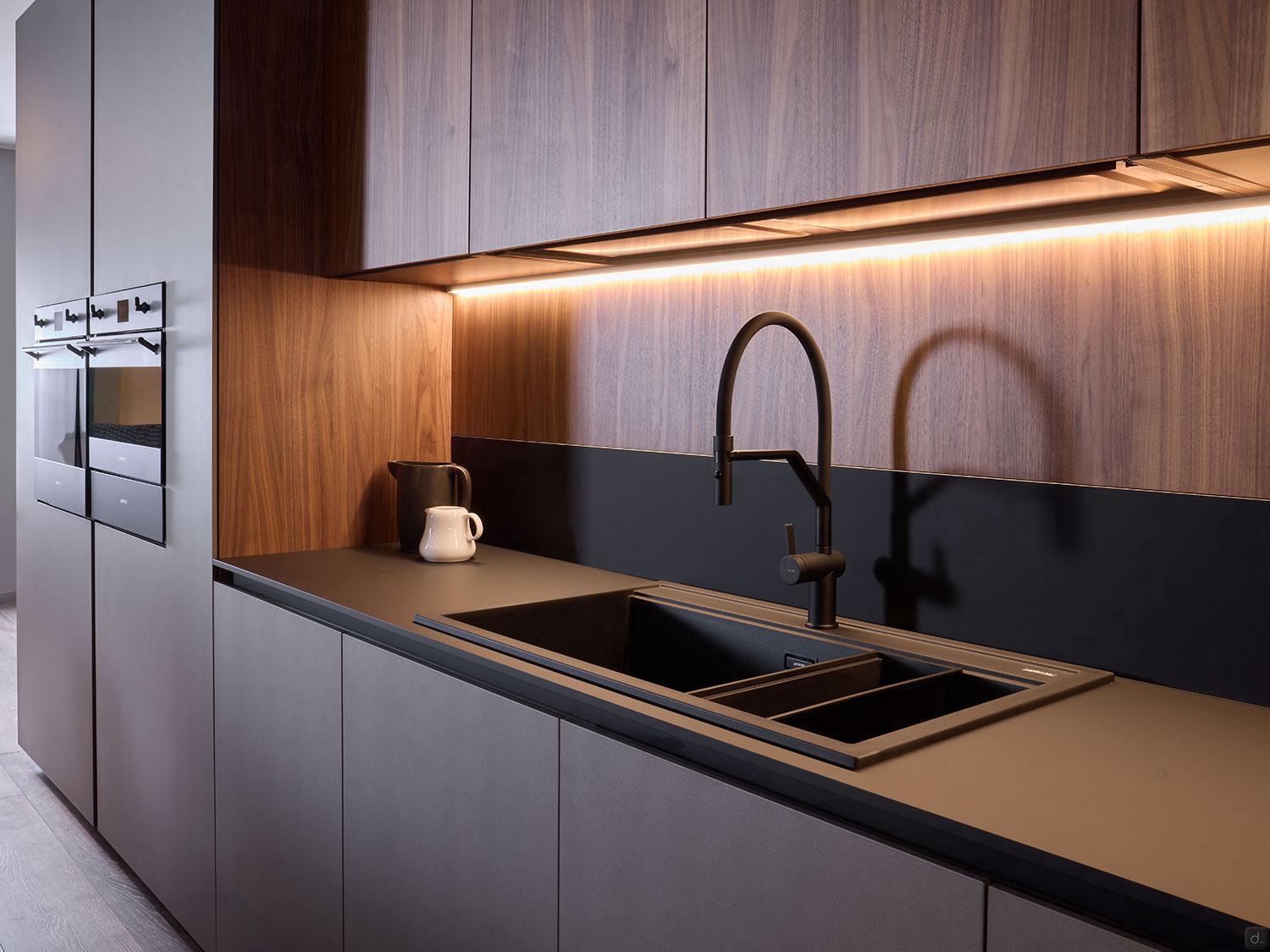 Modern Kitchens by Kitchen Furniture feature sleek wood cabinets, a matte black countertop, built-in ovens, and an integrated black sink with curved faucet—ideal inspiration for lovers of modern kitchens and custom kitchen furniture.