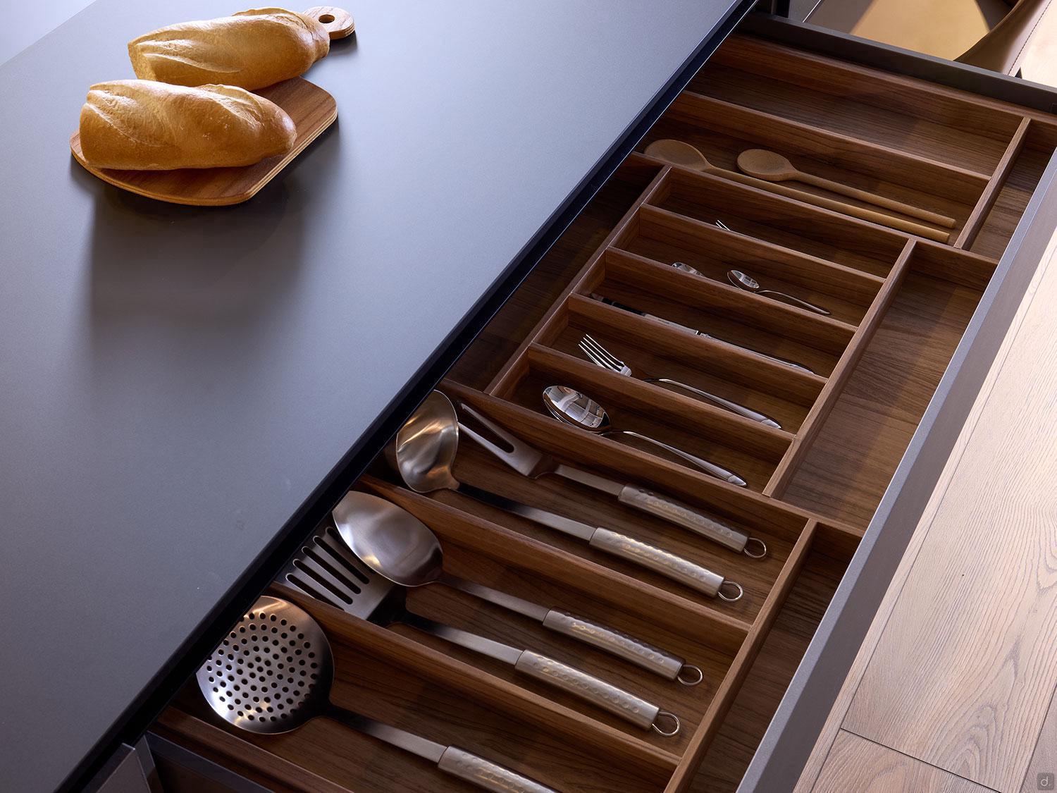 An open drawer from the Kitchen Furniture Modern Kitchens line reveals neatly organized wooden compartments with utensils, while two loaves of bread rest on a small cutting board atop the counter above.