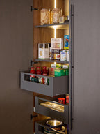 The Kitchen Furniture Modern Kitchens pantry features tall, open wooden shelves with built-in lighting, organized for jars, bottles, and groceries. Select shelves include pull-out drawers for easy access—ideal for contemporary kitchens.