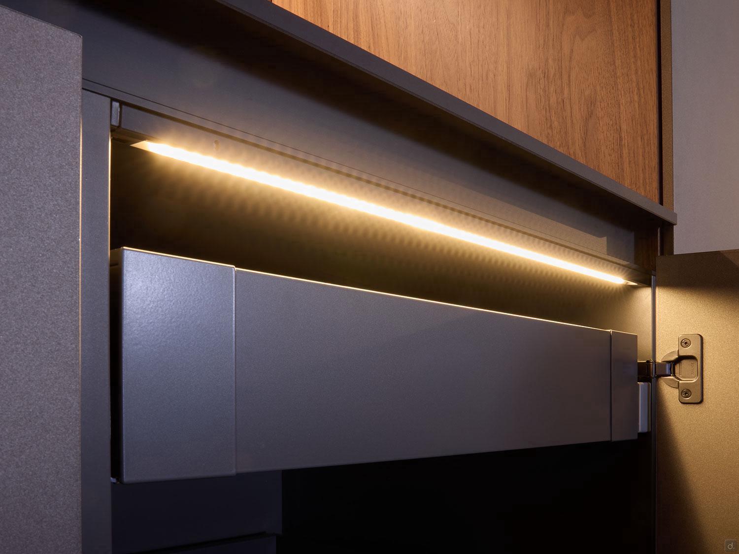 A close-up of an open drawer in the Modern Kitchens line by Kitchen Furniture, featuring a built-in LED strip light and sleek dark wood finishes for a stylish, contemporary look.