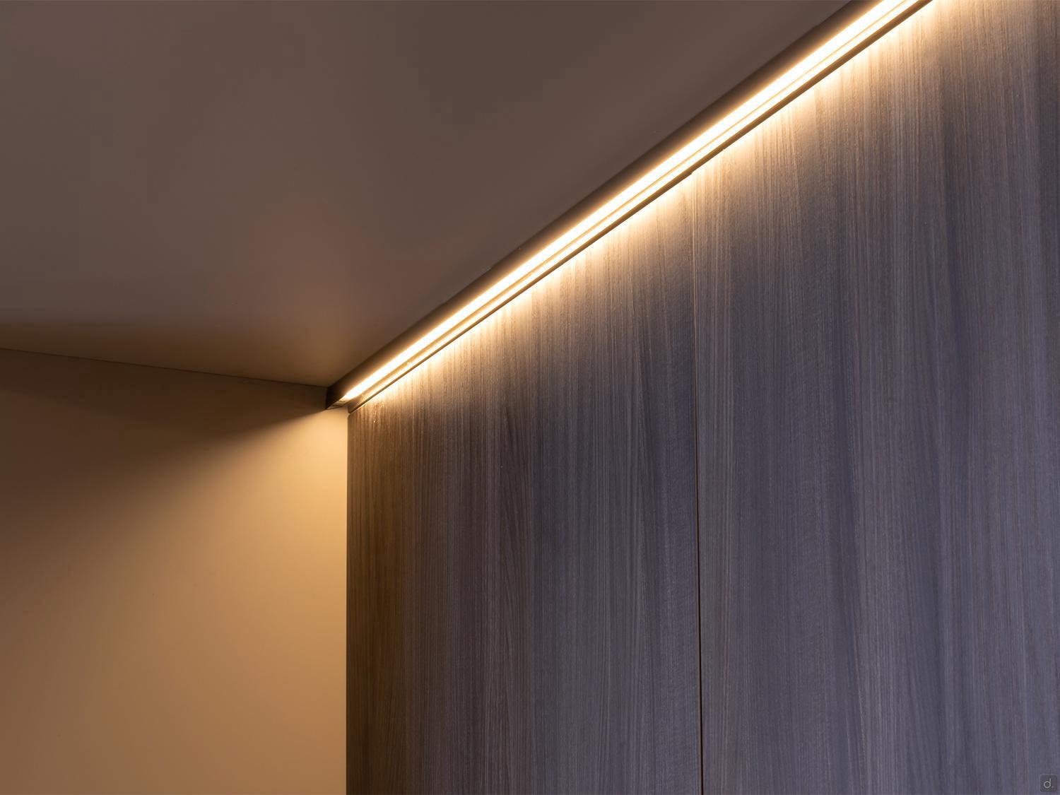 A warm white LED strip light illuminates smooth wood panels in a minimalist corner, creating a soft ambient glow—ideal inspiration for Modern Kitchens by Kitchen Furniture.