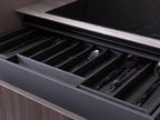 A Modern Kitchens drawer by Kitchen Furniture features a dark wood organizer neatly holding cutlery, adding sophistication beneath a sleek countertop and beside a black cooktop.