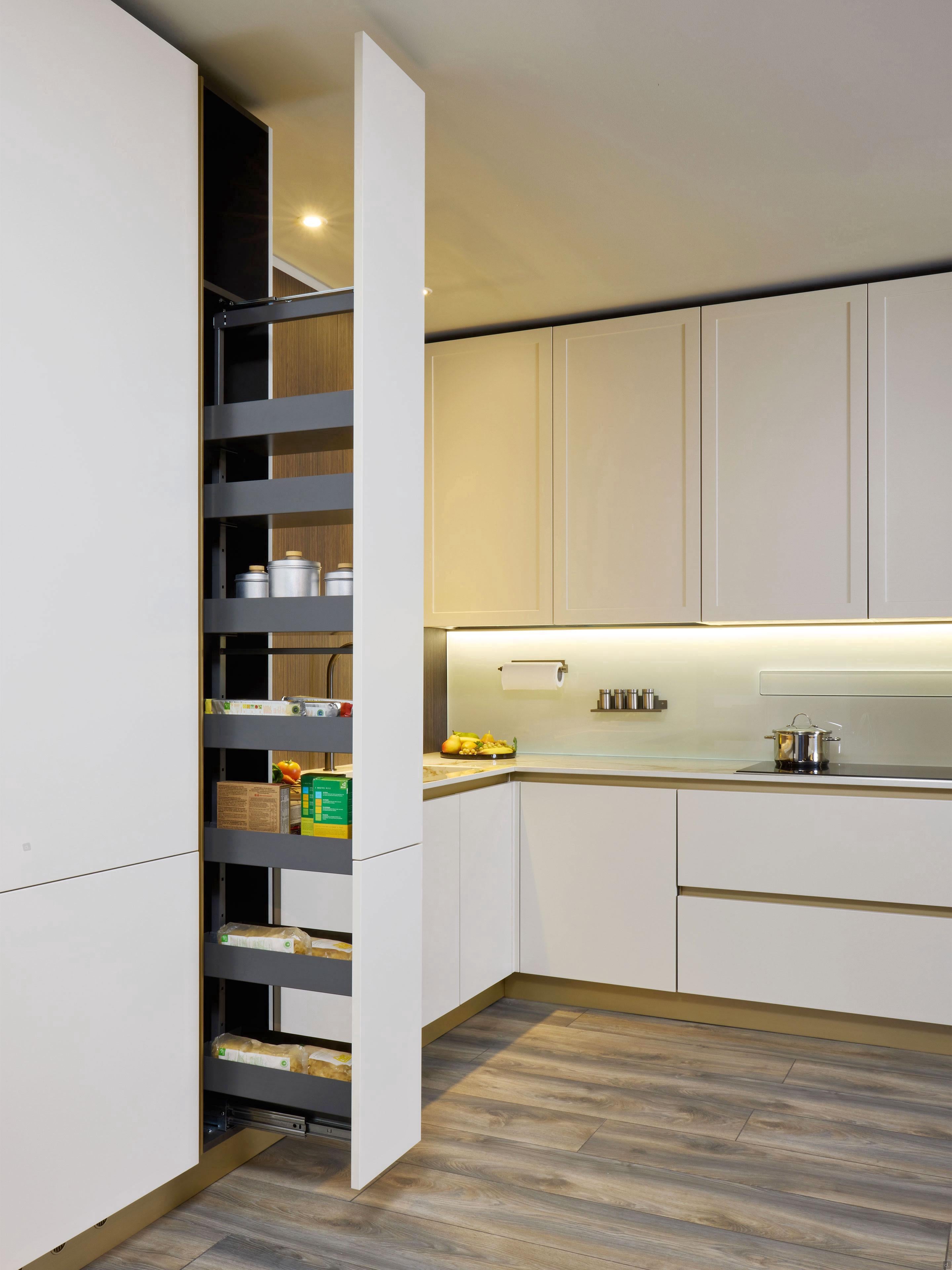 The Modern Kitchens by Kitchen Furniture features light cabinets, wood flooring, a tall pull-out pantry with shelves of jars, custom kitchen furniture, and under-cabinet lighting for a sleek, contemporary look.