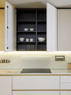 The Modern Kitchens collection by Kitchen Furniture features white open cabinets for displaying cups, bowls, and spices, a marble countertop, under-cabinet lighting, and sleek custom furniture for a clean, minimalist design.