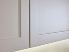 Close-up of two white recessed panel doors from the Modern Kitchens line by Kitchen Furniture, featuring clean edges and a narrow gap, softly illuminated along the lower edge.