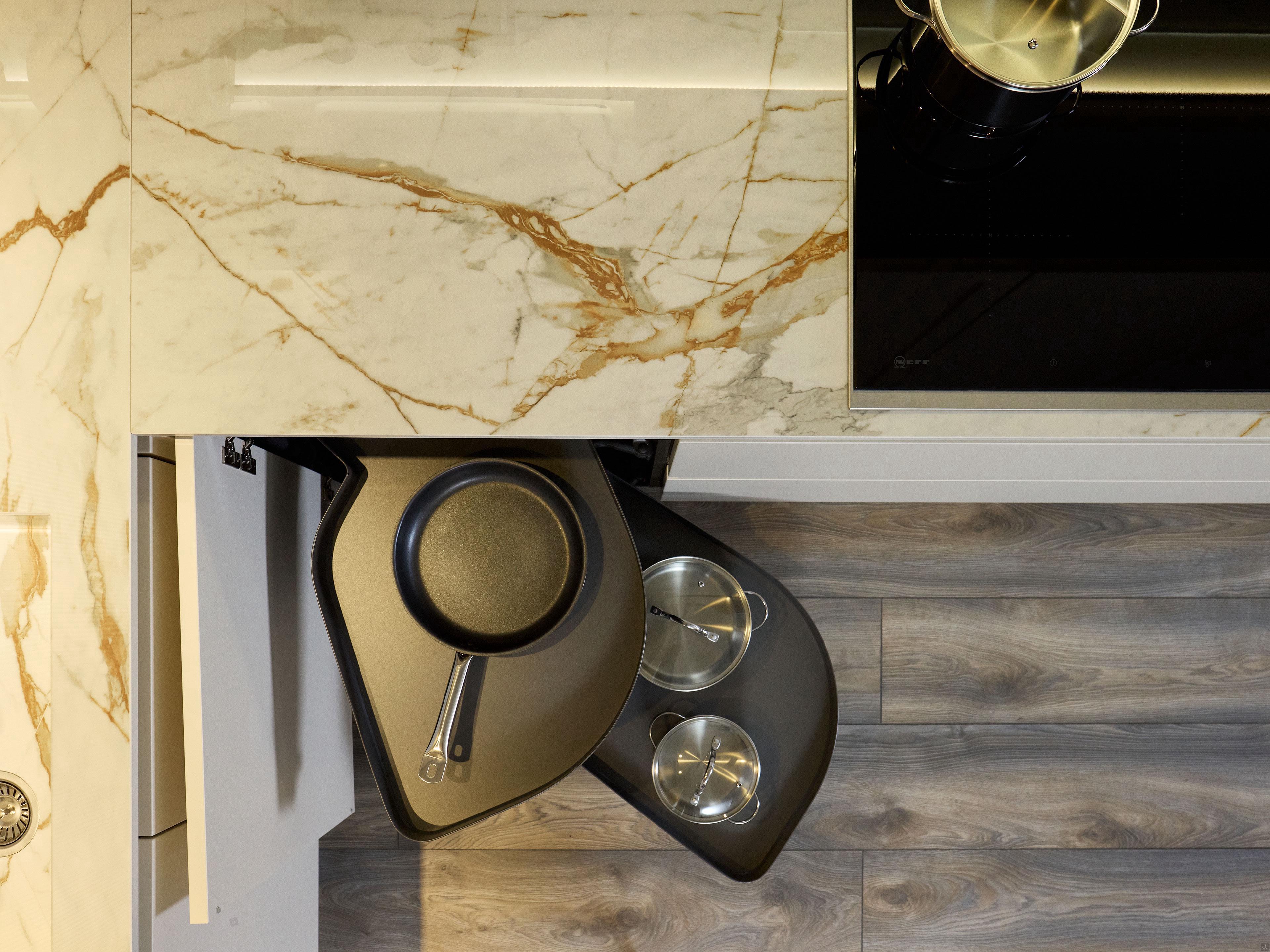 Overhead view of Modern Kitchens by Kitchen Furniture, featuring a marble countertop, induction cooktop with pot, and corner cabinet pull-out tray for cookware on wood-style flooring—exemplifying smart kitchen design.