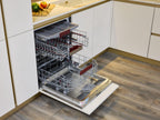 A Modern Kitchens built-in dishwasher by Kitchen Furniture stands open with empty racks and a cutlery tray, set in a space with white cabinets and wood flooring—ideal for highlighting stylish custom kitchen design.