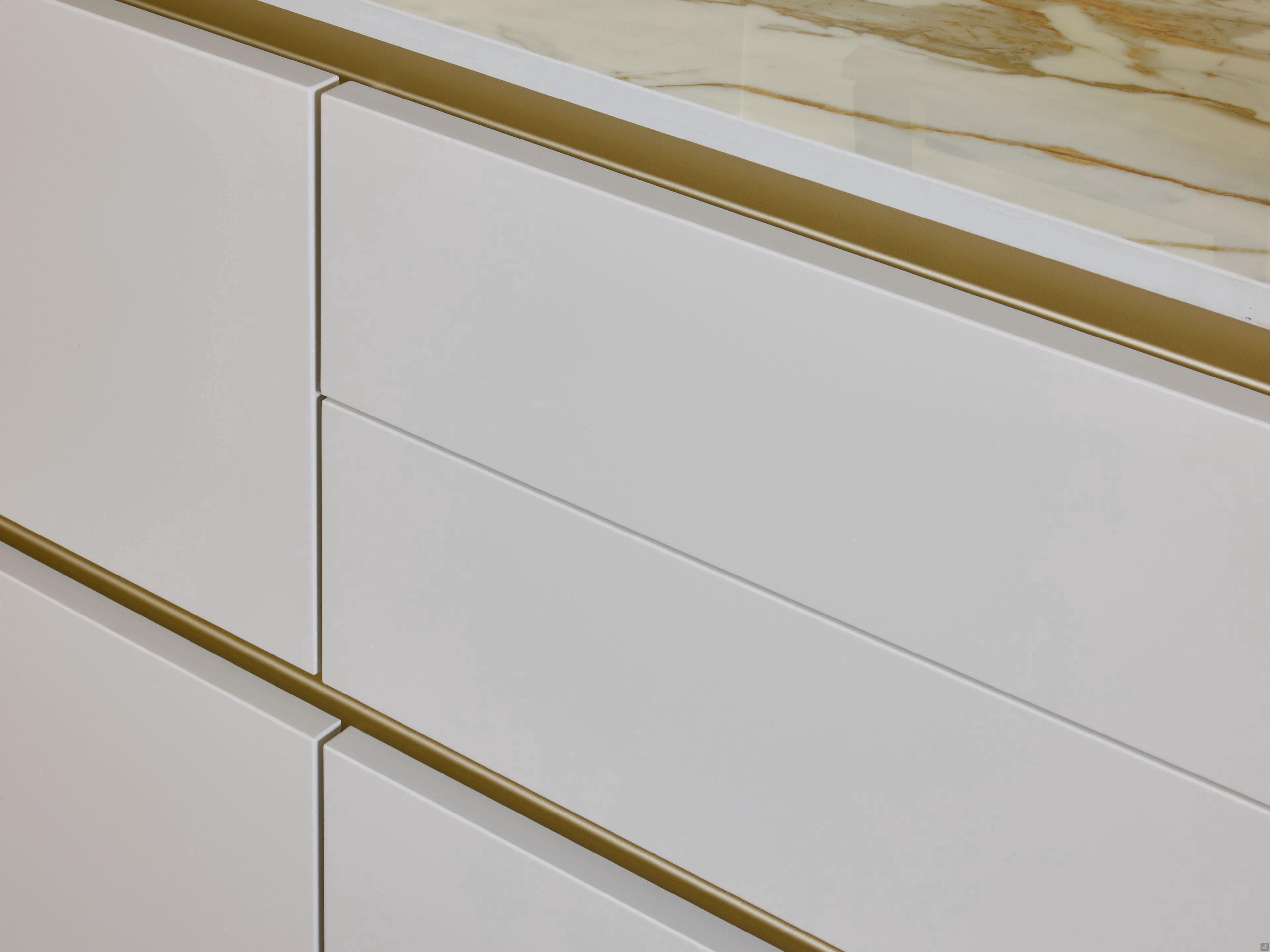 Close-up of Modern Kitchens by Kitchen Furniture, featuring drawers with sleek gold handles and a cream-and-brown marble countertop for an elegant kitchen design.