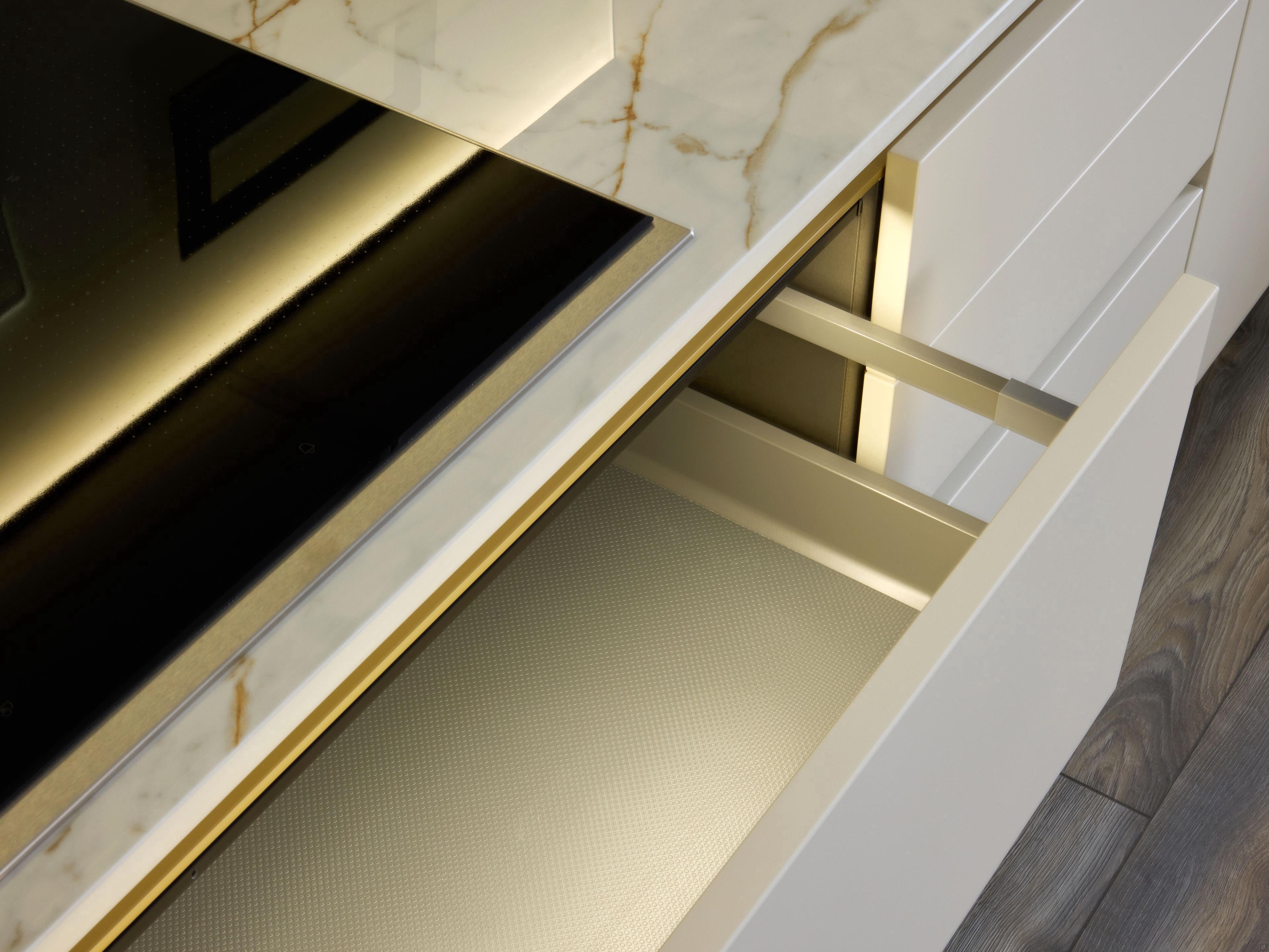 The Modern Kitchens countertop by Kitchen Furniture features a marble finish, an induction cooktop, and an open white drawer with a textured liner below, all set against a warm wood floor for an elegant kitchen design.