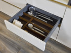A modern kitchen drawer by Kitchen Furniture features a wooden organizer holding utensils like a ladle, serving spoon, and slotted spoon—demonstrating the thoughtful design and organization of Modern Kitchens.