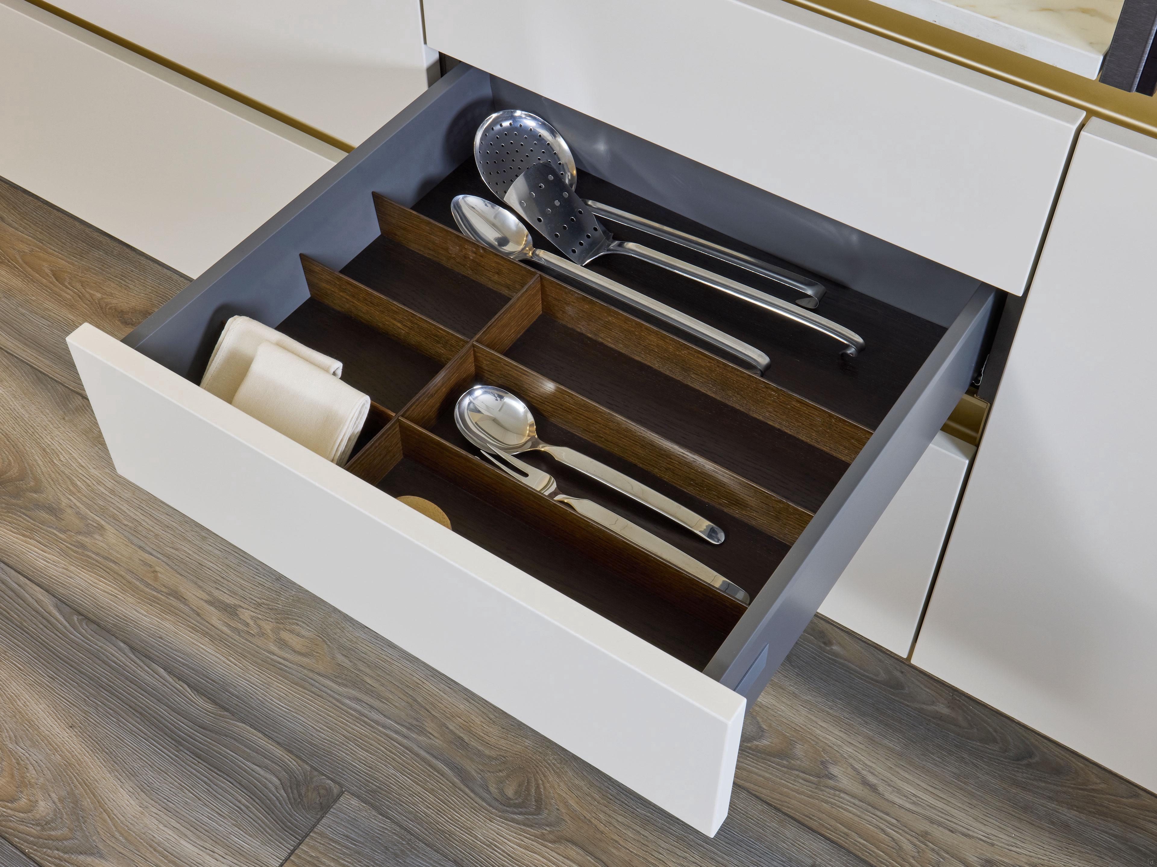 A modern kitchen drawer by Kitchen Furniture features a wooden organizer holding utensils like a ladle, serving spoon, and slotted spoon—demonstrating the thoughtful design and organization of Modern Kitchens.