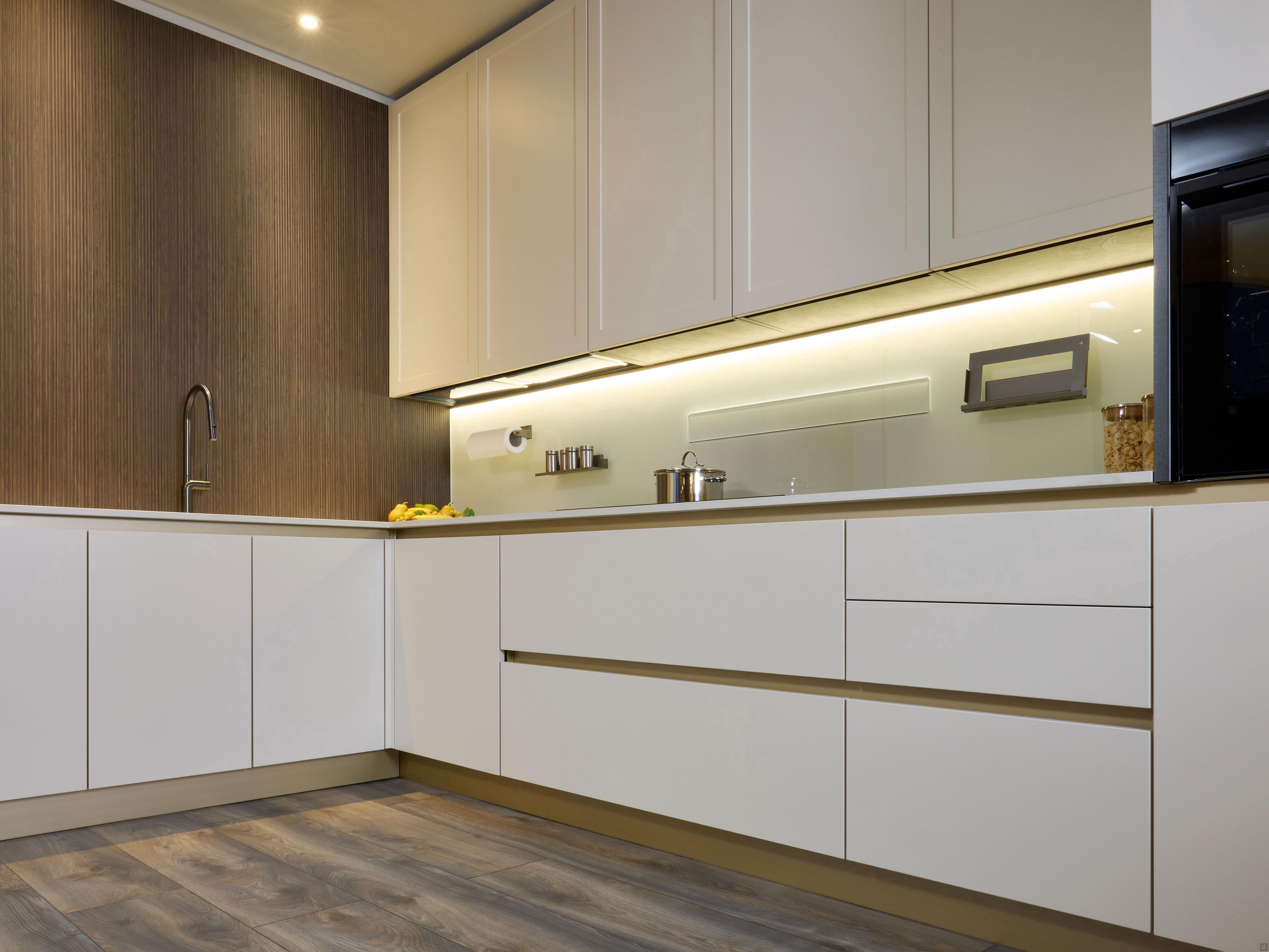 Modern Kitchens by Kitchen Furniture feature white cabinets, wood-textured backsplash, under-cabinet lighting, built-in oven, and wide gray planks, creating a minimalistic and stylish Yerevan-inspired modern kitchen.