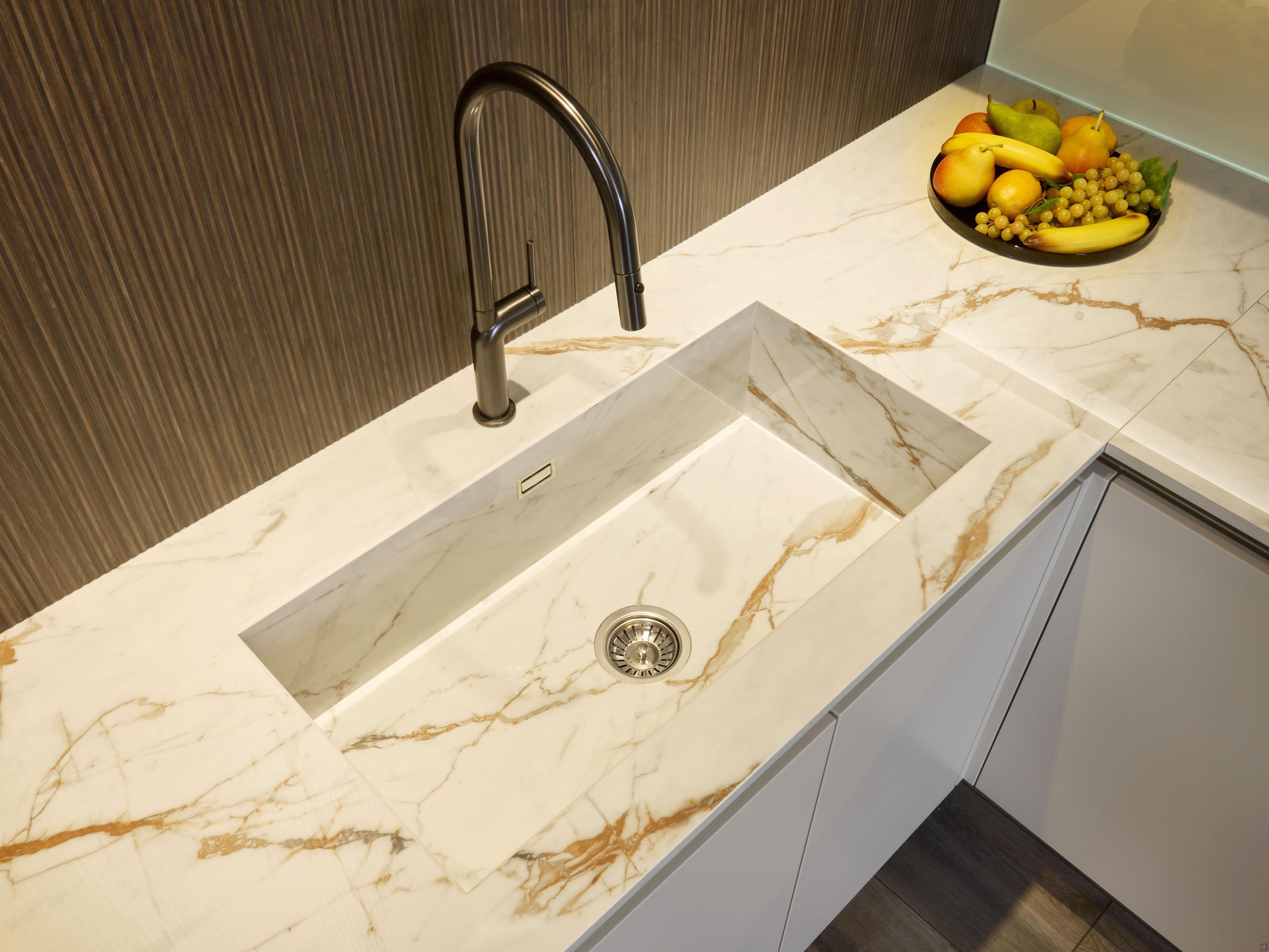 Close-up of a Modern Kitchens sink by Kitchen Furniture, featuring a marble countertop, stainless steel faucet, and a fruit bowl—highlighting elegant design and stylish custom kitchen furniture.