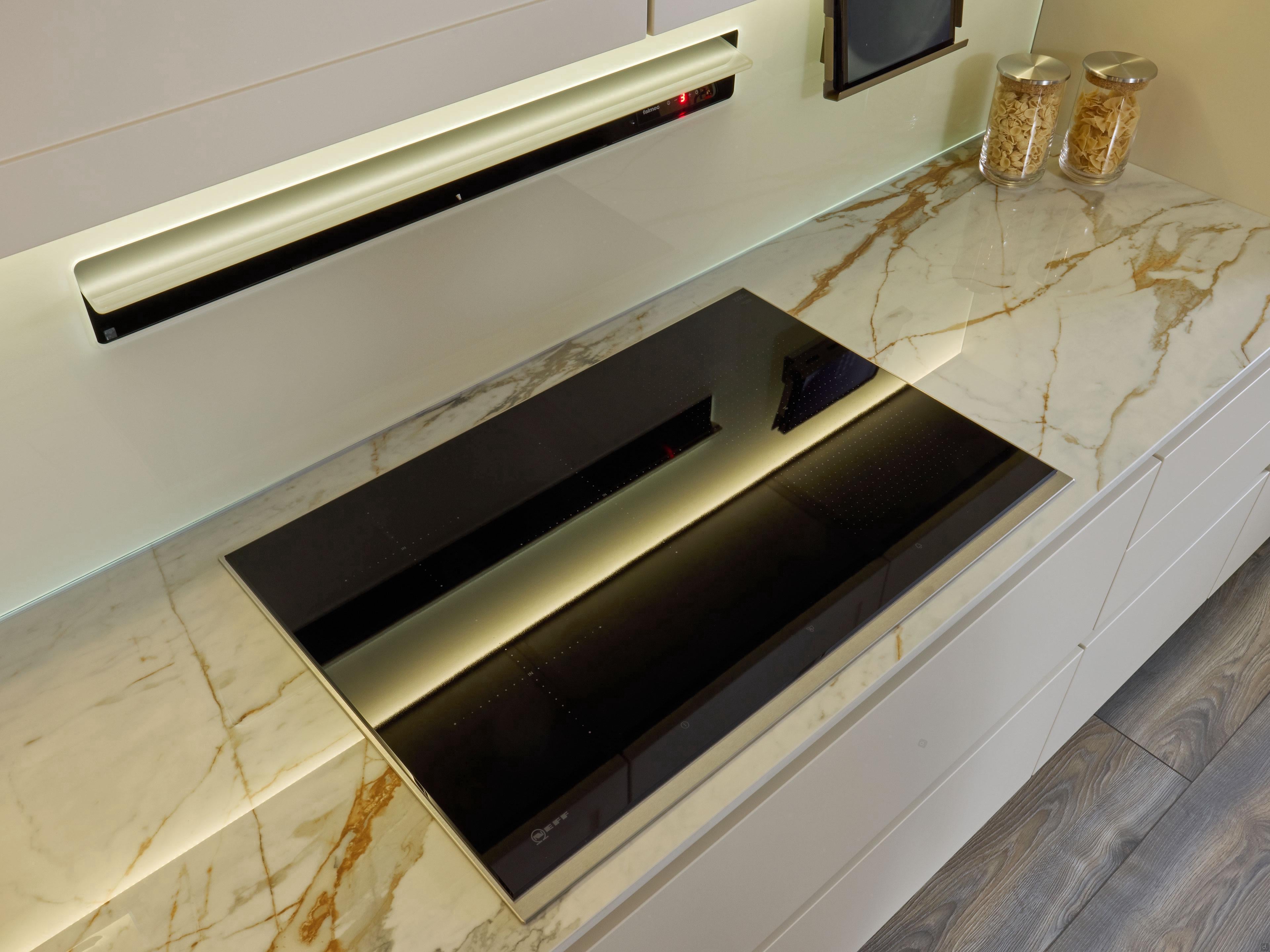 Modern Kitchens by Kitchen Furniture features a sleek black glass induction cooktop, white cabinets, marble-patterned surfaces, custom furniture, pasta jars, and under-cabinet lighting for a stylish culinary space.
