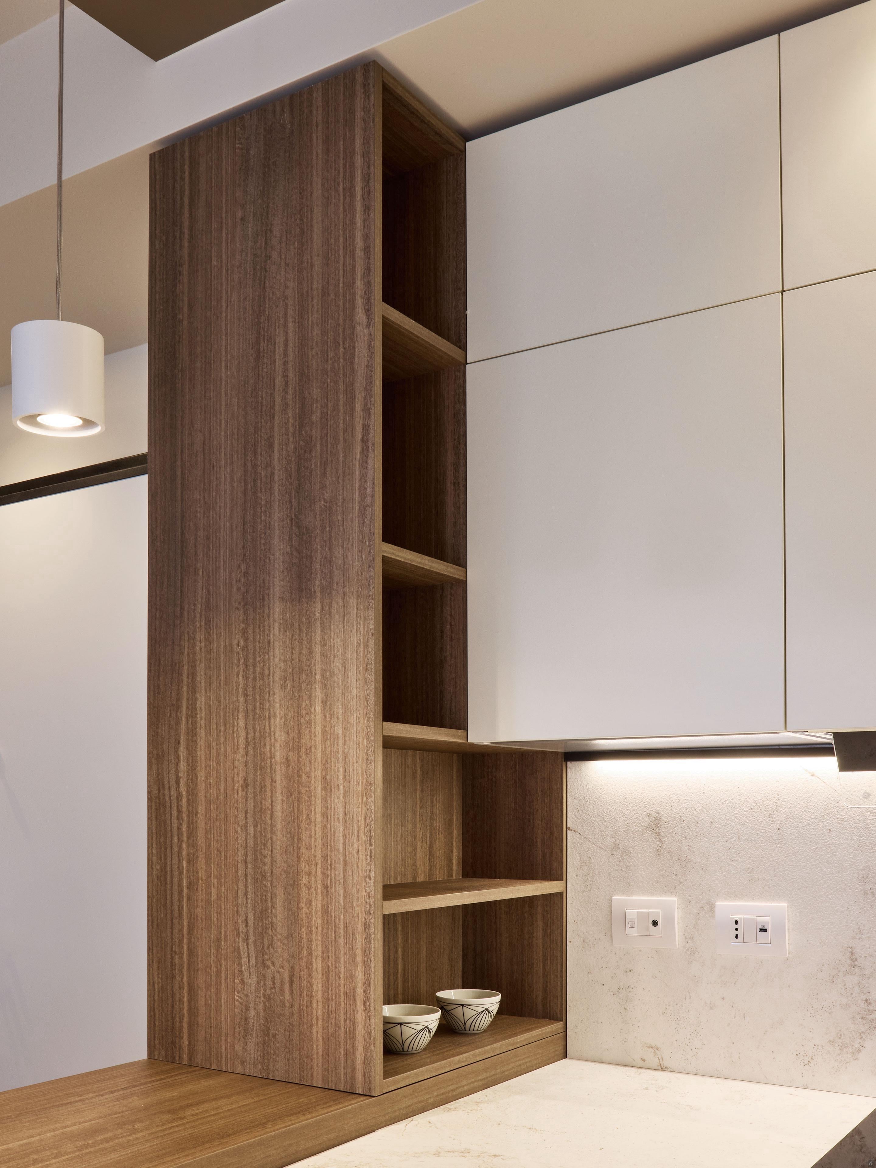 The Modern Kitchens by Kitchen Furniture features a Yerevan corner with vertical wooden open shelves beside white cabinets, two small bowls on the lower shelf, a light counter and backsplash, and two power outlets on the wall.