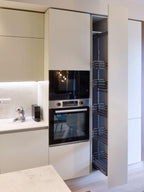 A Modern Kitchens setup by Kitchen Furniture in Yerevan features a built-in oven, microwave, and an open pull-out pantry with metal shelves—all set in sleek light cabinetry, countertop, and backsplash.