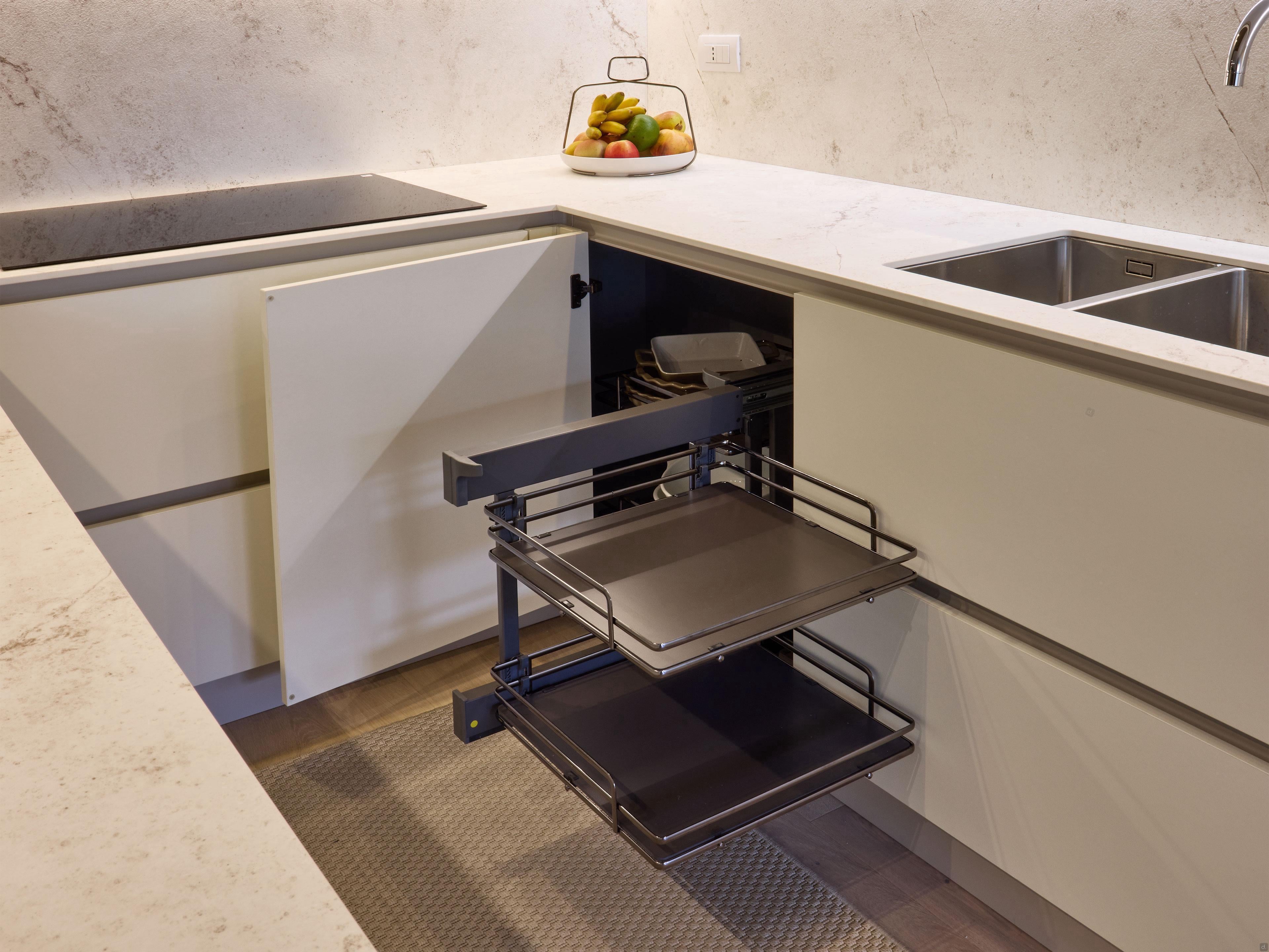 The Modern Kitchens corner cabinet by Kitchen Furniture is open, revealing a two-tier metal pull-out shelf. On the countertop sits a bowl of fruit next to a sink, emphasizing innovative kitchen design.