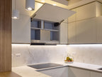 The Modern Kitchens by Kitchen Furniture in Yerevan features white cabinets, an open upper cabinet showing shelves and a ventilation duct, a white countertop with a fruit basket, built-in cooktop, and bright under-cabinet lighting.