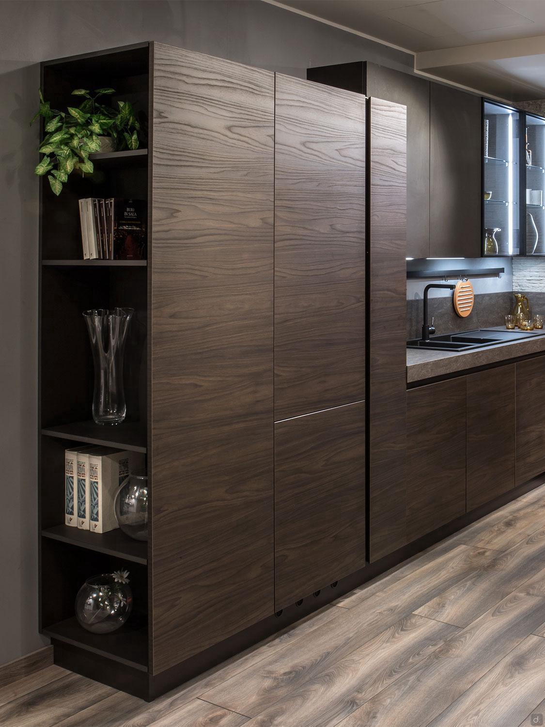 Urban Kitchens by ORDER Kitchen Furniture features a modern kitchen with dark wood cabinets, open shelving for books, plants, and decor, plus industrial elements that enhance the gray countertop and light wood floor.