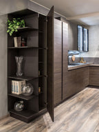 Urban Kitchens by ORDER Kitchen Furniture combines dark wood cabinets, custom pieces, and open shelving for decor and glassware. A tall cabinet conceals extra storage, while light wood floors and greenery add a warm, modern touch.