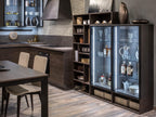 Modern kitchen features dark wood cabinets, a four-seat dining table, glassware display, sleek surfaces, open shelves, and under-cabinet lighting. Custom kitchen furniture inspired by "Urban Kitchens" from ORDER Kitchen Furniture.