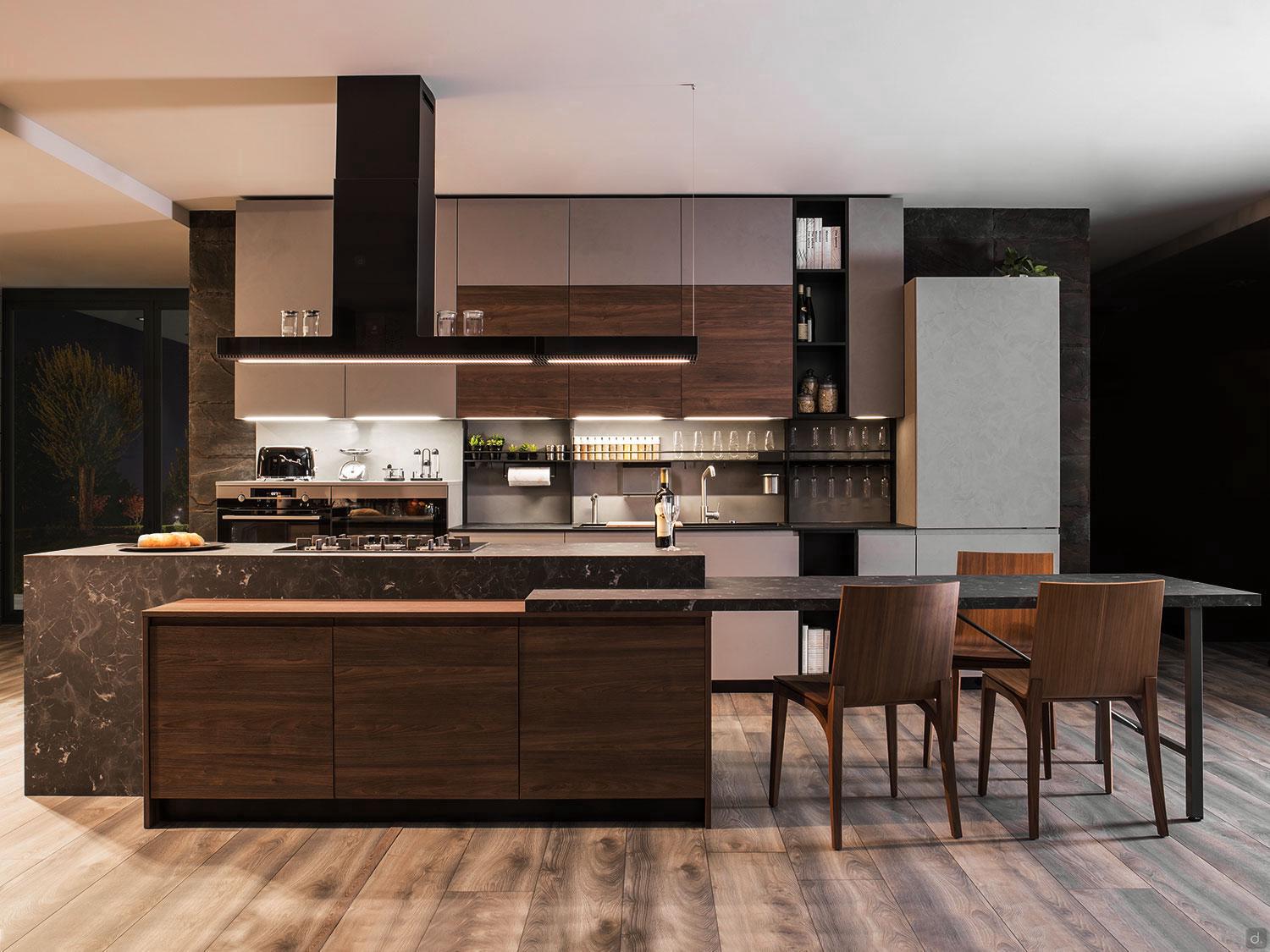 The Urban Kitchens by ORDER Kitchen Furniture features dark wood cabinets, marble countertops, built-in appliances, open shelves with glassware, under-cabinet lighting, and a dining area with two wooden chairs on wood flooring.
