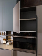 A modern Yerevan kitchen features an open cabinet with two empty shelves above a built-in Whirlpool oven. Nearby, a bottle of wine, scale, and spice jars rest on the countertop by Kitchen Furniture's Urban Kitchens line.