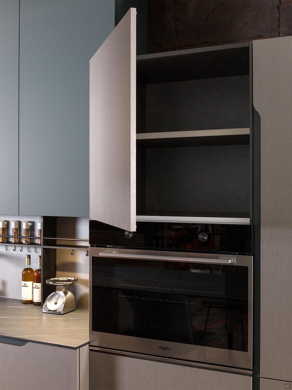 A modern Yerevan kitchen features an open cabinet with two empty shelves above a built-in Whirlpool oven. Nearby, a bottle of wine, scale, and spice jars rest on the countertop by Kitchen Furniture's Urban Kitchens line.