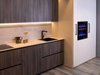 Urban Kitchens by Kitchen Furniture feature dark wood cabinets, a light stone backsplash, sleek black sink, under-cabinet lighting, and a white appliance unit with built-in oven or wine cooler—urban kitchen inspiration.